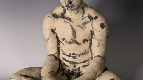 Decorated ceramic male figure seated, looking contemplatively down.